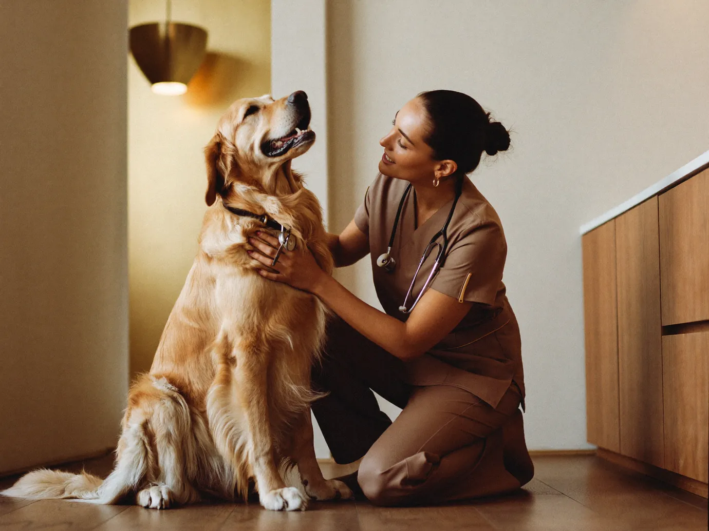 A vet in taupe scrubs greeting a golden retriever